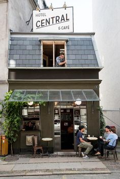 two men sitting at tables in front of a building with a sign that reads central cafe