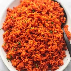 a white plate topped with red rice and a black spoon on top of a table