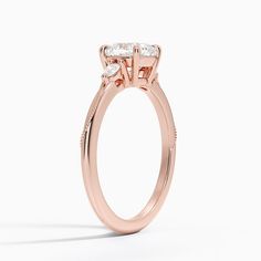 a rose gold engagement ring with three stones on the side and an oval diamond center