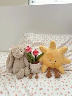 two stuffed animals sitting on top of a bed next to flowers and a potted plant