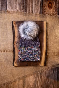 a knitted hat with a fur pom sits on top of a piece of wood