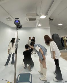 several people are taking pictures in an empty room with white walls and lighting equipment on the floor