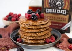 a stack of pancakes topped with berries and syrup next to a bottle of kodak cakes