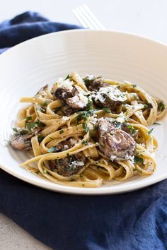 pasta with mushrooms and parmesan cheese in a white bowl on a blue napkin