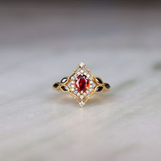 a gold ring with a red stone surrounded by black and white stones on a table