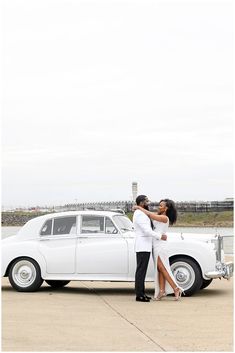 a man and woman kissing in front of a white car