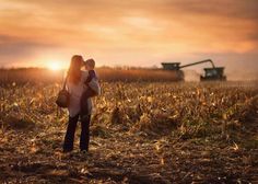 a woman holding a baby in her arms while standing in a field with a tractor behind it