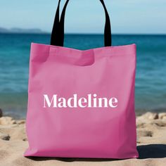 a pink bag with the word madeline on it sitting in the sand at the beach