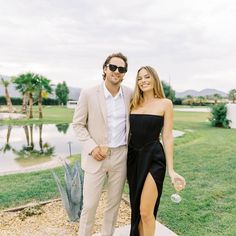 a man and woman standing next to each other in front of a lake with palm trees