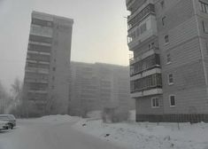 the cars are driving down the snow covered road in front of tall buildings on either side of the street