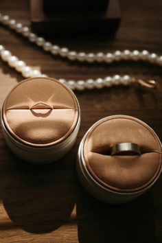 two ring boxes sitting on top of a wooden table next to a pearl necklace holder