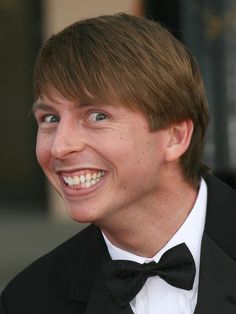 a young man in a tuxedo smiles at the camera while wearing a black bow tie