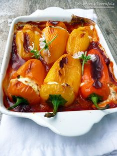 a white dish filled with stuffed peppers covered in sauce