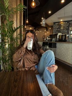 a woman sitting at a table drinking from a cup with her feet up on the table