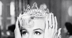 a black and white photo of a woman wearing a tiara with her hands on her head