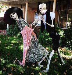 two skeletons dressed up in halloween costumes holding hands and walking through the yard with their heads held back