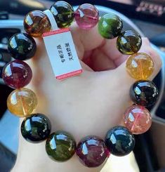 a person holding up a bracelet made out of multicolored glass beads with a tag on it