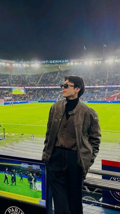 a man standing in front of a tv at a soccer stadium with the lights on