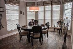 a dinning room table and chairs in front of two windows with blinds on them