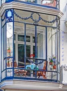 a balcony with blue iron railings and chairs on the windowsill in front of an apartment building