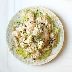 a white plate topped with chicken and lettuce covered in ranch dressing on top of a table