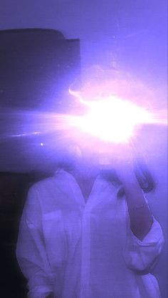 a man in white shirt standing next to a wall with purple light coming from his head