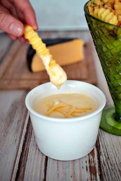 a person dipping cheese into a bowl of soup with a green grater on the side