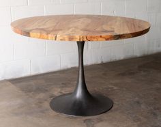 a round wooden table sitting on top of a cement floor next to a white brick wall