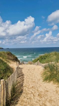 a sandy path leading to the ocean on a sunny day with clouds in the sky