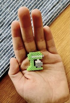 a person's hand holding a small green and white letter t brooch in their left hand