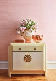 a vase with flowers on top of a small cabinet in front of a pink wall