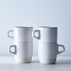 two white coffee mugs sitting on top of each other in front of a wall