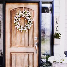 a wooden door with a wreath on the front and side of it next to potted plants