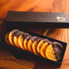 chocolate covered orange slices in a black box on a wooden table with wood grained surface