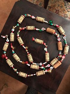 a wooden table topped with a beaded necklace on it's side and two wine corks attached to the beads