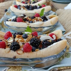 three banana split desserts with berries and nuts in them on a glass platter