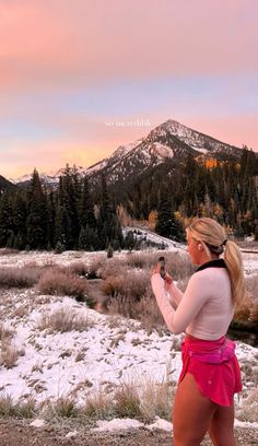 a woman is standing in the snow with her cell phone