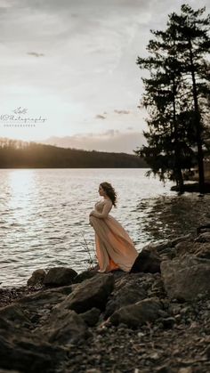 a woman standing on rocks near the water at sunset with her back to the camera