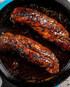 two meats cooking in a skillet on the stove top, with sauce and seasoning