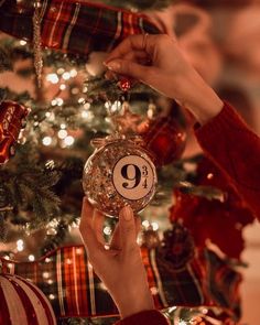 two hands holding up a christmas ornament in front of a decorated christmas tree