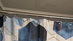 a curtain with blue and white designs hanging from it's metal rod in front of a window