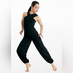 a woman in black jumpsuits is posing with her hands behind her back and one foot on the ground