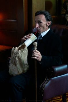 a man sitting in a chair drinking from a paper bag while holding a wine bottle