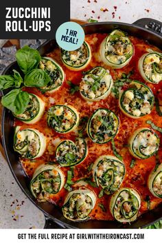 zucchini roll ups in a skillet with spinach leaves on top