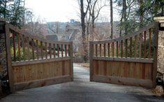 two wooden gates open on a driveway with trees in the background