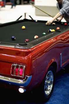 a man is playing pool in an old red mustang muscle car with billiards on it