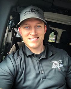 a man wearing a hat sitting in the back seat of a car smiling at the camera