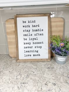 a wooden sign sitting on top of a counter next to a potted plant