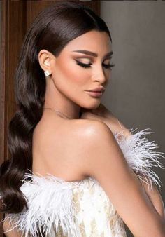 a woman with long dark hair wearing a white feathered dress and holding her hand on her shoulder