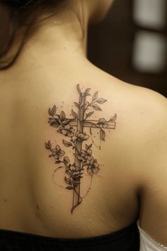 the back of a woman's shoulder with a cross and flowers tattoo on it